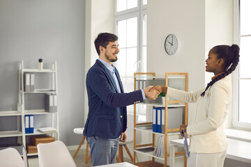 Happy manager getting acquainted and exchanging handshake with new client. Two diverse business people meet in office, shake hands, make agreement and thank each other for help and cooperation