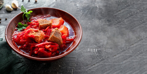 Red borsch with vegetables and meat in a clay plate. Steam from hot tomato soup. Dark background. Delicious healthy lunch. Copy space