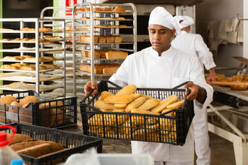 Baker with box with baguettes in bakery kitchen