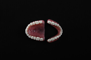 Full removable plastic denture of the jaws. A set of dentures on a black background. Two acrylic dentures. Upper and lower jaws with fake teeth. Dentures or false teeth, close-up. Copy space