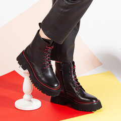 Women's legs in black pants and black short shoes on medium heel stands in the studio against a colored background