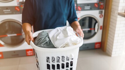 Man doing launder holding basket with dirty laundry of the washing machine in the public store. laundry clothes concept