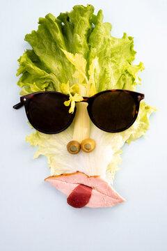 creative concept, cubist style portrait made from lettuce, apio, pastrami and olives, with sun glasses, isolated on white