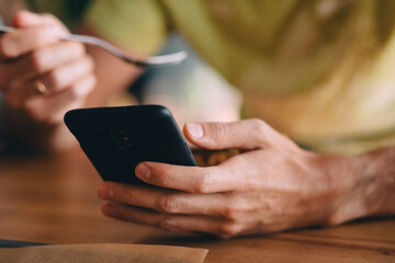 Guy using phone while eating, close view of hands using black phone