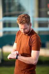 Young sporty ginger man looking at the watch after exercising outdoors.