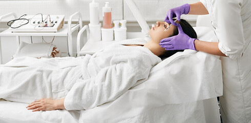 Attractive woman getting anti-aging injections into face area to remove facial wrinkles at a beauty...
