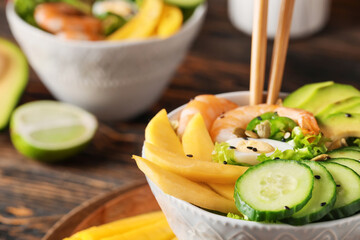 Bowl of fresh salad with mango, shrimps and vegetables on wooden background, closeup