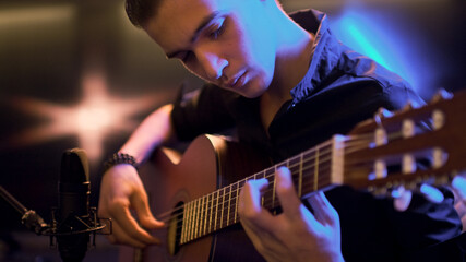 Obraz premium Man plays guitar. Young man plays a musical instrument. Musician records his composition in a music Studio using professional microphone