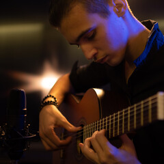 Obraz premium Man with a classical guitar in a neon glow. Teenager plays guitar. Young man plays a musical instrument.