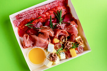 White dish with carpaccio of beef in white delivery box, take away concept. Over bright green...