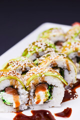 Uramaki sushi roll with smoked eel and unagi on white plate over black background. Japanese cuisine concept.