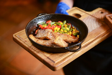 Delicious meat and veggies dinner in dark round pan served by waiter in restaurant or diner.