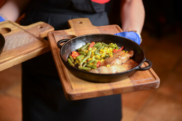 Delicious meat and veggies dinner in dark round pan served by waiter in restaurant or diner.