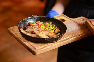 Delicious meat and veggies dinner in dark round pan served by waiter in restaurant or diner.
