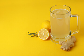 Glass of ginger beer and ingredients on yellow background