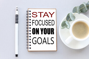 stay focused on your goals. text on white notepad paper. near cups with coffee and plants on a gray background.
