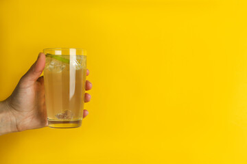 Female hand hold glass of ginger beer on yellow background