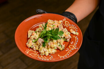 Russian traditional salad Olivier served by waiter in restaurant or diner. Vegetable mayonnaise...