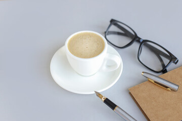 gray background with coffee cup, pen and glasses. Top view with copy space