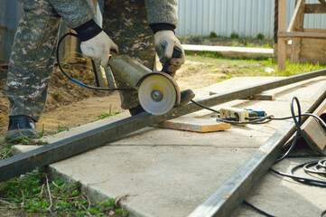 close-up - worker cuts a metal profile with a grinder, hands in protective white gloves