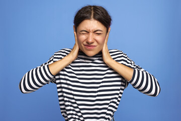 Isolated image of irritated unhappy young woman wearing nose ring closing eyes, covering ears with hands, protecting them from loud sound or noise, suffering from infection, having sharp pain