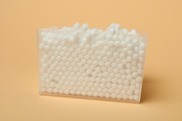 Plastic box with cotton swabs on beige background