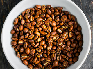 Coffee beans in a white plate on wooden background.