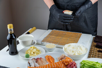 Close up of sushi chef hands preparing japanese food. Man cooking sushi at restaurant. Traditional asian seafood rolls on cutting board.