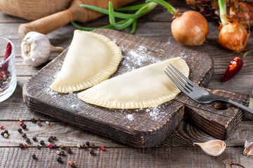 Raw chebureks on a wooden background. The concept of home baking with raw dough and minced meat