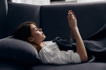 red-haired woman lies on a pillow on the couch with a mobile phone in her hand
