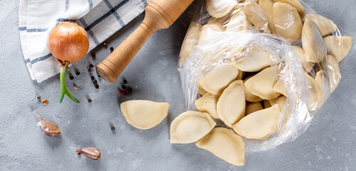 Traditional Russian dumplings, ravioli, meat dumplings on a light concrete background. Rolling pin, napkin, garlic, onion, bay leaf and spices. View from above. Copy space. Banner