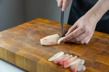 Close up of Chef cook hands chopping salmon fish for traditional Asian cuisine with Japanese knife. Professional Sushi chef cutting seafood for rolls.