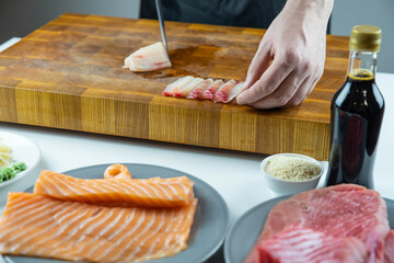 Close up of Chef cook hands chopping salmon fish for traditional Asian cuisine with Japanese knife. Professional Sushi chef cutting seafood for rolls.