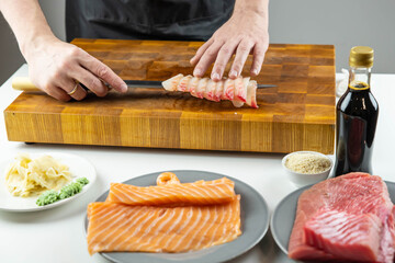 Close up of Chef cook hands chopping salmon fish for traditional Asian cuisine with Japanese knife. Professional Sushi chef cutting seafood for rolls.