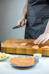 Close up of Chef cook hands chopping salmon fish for traditional Asian cuisine with Japanese knife. Professional Sushi chef cutting seafood for rolls.