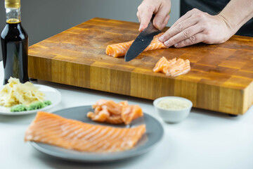 Close up of Chef cook hands chopping salmon fish for traditional Asian cuisine with Japanese knife. Professional Sushi chef cutting seafood for rolls.