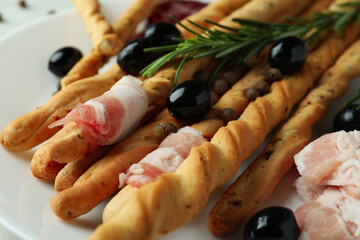 Tasty grissini with bacon and snacks, close up