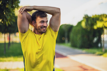 Young man is exercising outdoor. He is stretching his body and warming up for jogging.