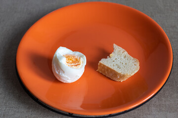 a nibbled piece of white bread and a nibbled boiled egg on an orange plate