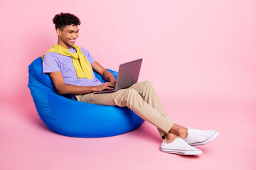 Full size photo of young handsome happy smiling afro man sit armchair working in laptop isolated on pink color background