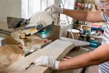 Side view of carpenter cutting with  radial arm saw. Woodworker using electric jigsaw in workshop for  production of wooden furniture. Joinery work concept. Close up