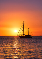 Silhouette of sailing boat with sails down against sun at sunset, sun glare on sea waters. Romantic seascape. Lifestyle landscape, skyline sailboat