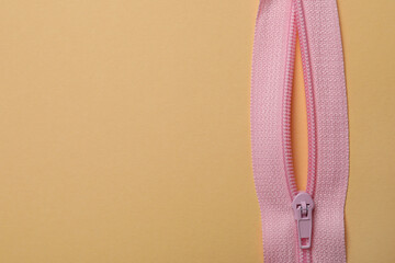 Pink zipper on beige background, close up