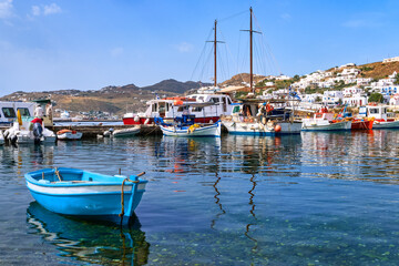 Fototapeta na wymiar Beautiful summer day in typical marina of Greek island. Fishing boats, yachts by jetty. Whitewashed houses. Small boat. Mykonos, Cyclades, Greece.