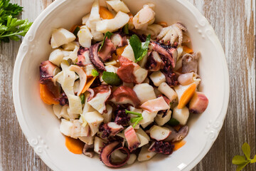 Seafood salad dressed and served in porcelain bowl on wooden background