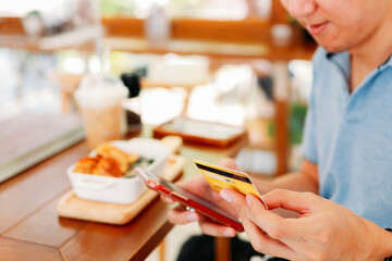 Closeup of hands of handsome young Asian man making card payment using smartphone while eating lunch in modern cafe with social distancing norms due to coronavirus
