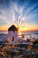 Famous traditional white windmill overlook port and harbor of Mykonos, Cyclades, Greece at sunset...
