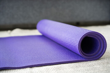 Rolled purple yoga exercise mat on the floor in living room close up