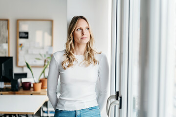 Serious young woman standing deep in thought looking through a window
