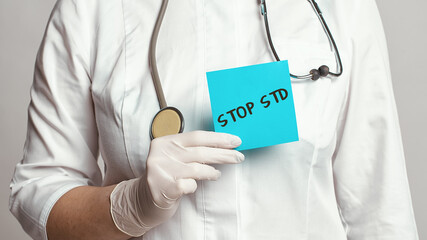 Cropped view of doctor in a white coat and sterile gloves holding a note with text - STOP STD